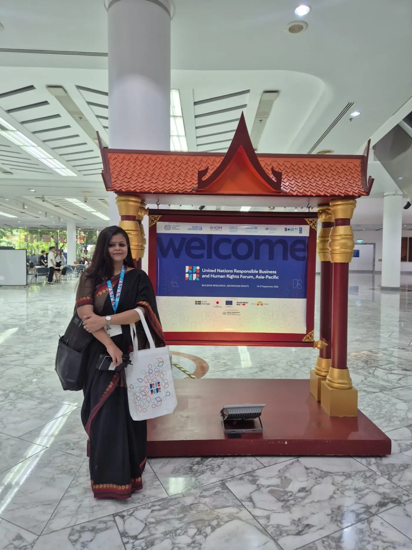 Anumita Sarkar standing at the welcome sign of the UN Responsible Business and Human Rights Forum, Asia-Pacific 2026, Bangkok